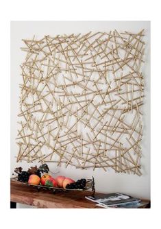 an art piece made out of sticks and fruit in front of a wall hanging on the wall