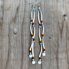 two white and blue beads are hanging from the side of a pair of silver earrings