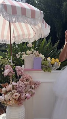 a woman standing under an umbrella next to a table with flowers and fruit on it