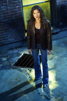 a woman standing in front of a brick building wearing jeans and a black blazer