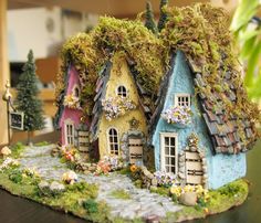 a miniature house with moss growing on it's roof and two trees in the background