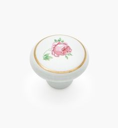 a white cabinet knob with a pink rose painted on the front and gold trimming