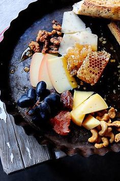 a plate full of different types of cheeses and nuts on a wooden table top