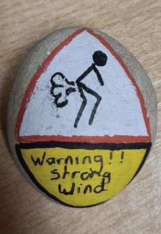 a painted rock with a stick figure on it that says warning wrong wind in black ink