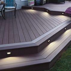 an outdoor deck with lights on it and flowers in the foreground, next to a patio