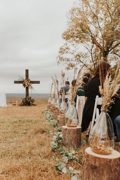 a group of people sitting in front of a cross on top of a grass covered field