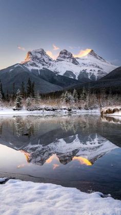 the mountains are covered in snow and there is a lake with water on it, surrounded by trees