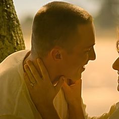 a man and woman standing next to each other in front of a tree with their faces close together