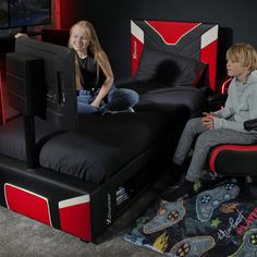 two children sitting on beds in a room with black and red accents, one boy is playing video games