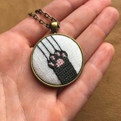 a hand holding a cross stitch necklace with a black cat on it