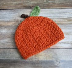 an orange crocheted hat sitting on top of a wooden floor next to a piece of wood