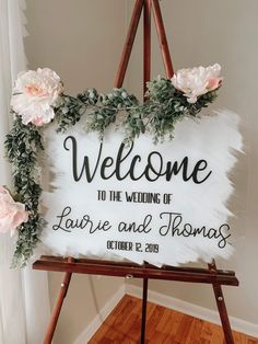 a welcome sign with flowers and greenery hanging from it's sides on a easel