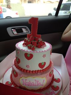 a pink and white cake with strawberries on it in the back seat of a car