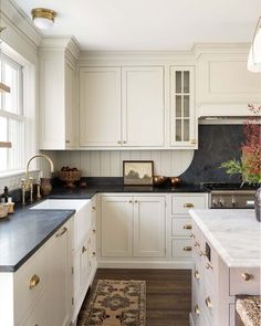 a white kitchen with black counter tops and gold pulls on the cabinet door knobs