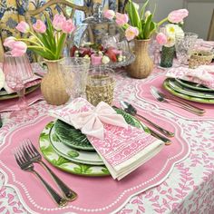 the table is set with pink and green plates, silverware, and napkins