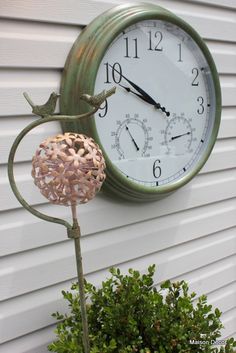 a clock mounted to the side of a white building next to a potted plant