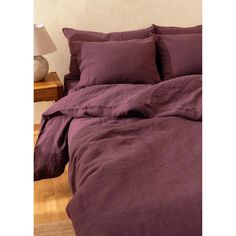 a bed with purple sheets and pillows on top of wooden flooring next to a night stand