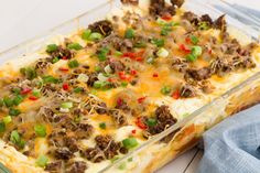 a casserole dish with meat, cheese and green onions in it next to a blue napkin