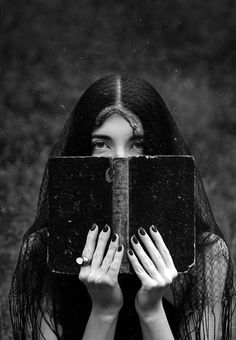 a woman with long black hair covering her face behind an open book in front of her face