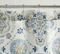 a curtain with blue and white flowers hanging from it's metal rod, in front of a tiled wall