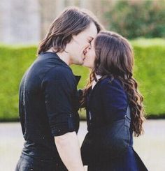 a man and woman kissing each other in front of bushes