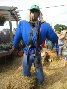 a scarecrow wearing a hat and scarf standing in hay bales with people around