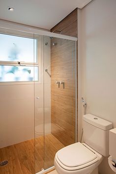 a white toilet sitting next to a shower in a bathroom with wooden floors and walls