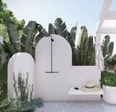 an outdoor shower with plants and a hat on the bench next to it in front of a white wall