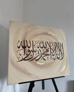 a painting with arabic writing on it sitting on top of a easel in front of a white wall