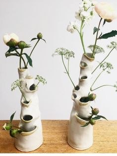 three white vases with flowers in them sitting on a wooden table next to each other