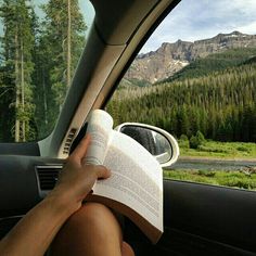 a person is reading a book in the back seat of a car while traveling through mountains