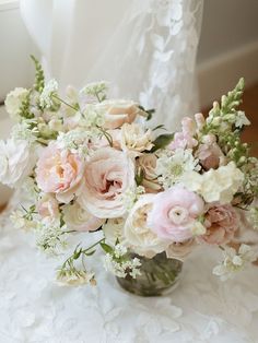 a vase filled with lots of pink and white flowers on top of a lace covered table cloth