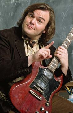 a man holding an electric guitar in front of a chalk board wall with writing on it