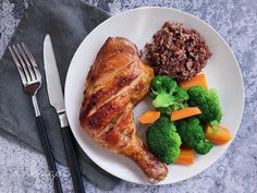 a white plate topped with meat and veggies next to a knife and fork