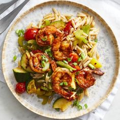 pasta with shrimp, zucchini and tomatoes on a plate next to a fork