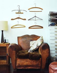 a brown chair sitting in front of a white wall with lots of hangers on it