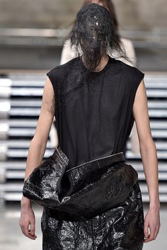 a man walking down a runway carrying a black bag on it's back legs