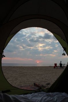 the sun is setting over the ocean from inside a tent on the beach with people sitting in chairs