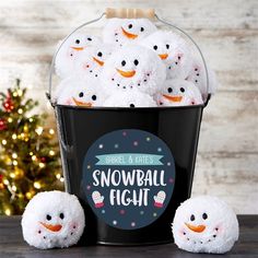 a bucket filled with snowballs sitting on top of a table next to a christmas tree