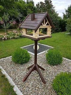 a bird house on a stand in the middle of some rocks and gravel with bushes around it