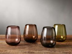 four different colored glass vases sitting on top of a wooden table next to each other