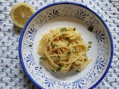 a white and blue plate topped with pasta next to a slice of lemon on a table