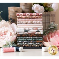 a stack of different colored papers next to pink flowers and other items on a table