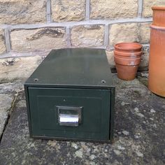 a green box sitting on top of a stone floor next to two potted plants