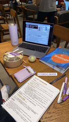 an open laptop computer sitting on top of a wooden table next to a notepad