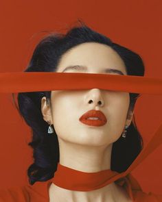 a woman with red lipstick covering her face behind a red ribbon and looking at the camera