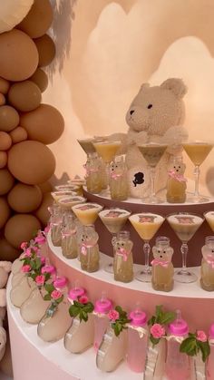 a teddy bear sitting on top of a table filled with drinks and desserts next to balloons