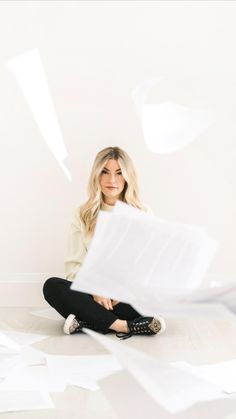 a woman sitting on the floor with papers flying around her