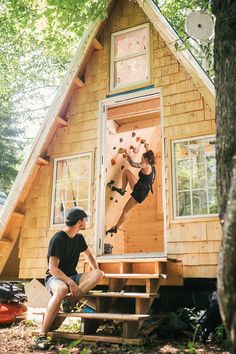 two people are climbing up the side of a house in the woods, while another person is sitting down