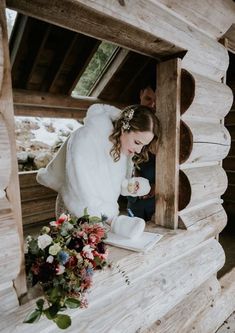 a woman in a fur coat standing next to a flower bouquet on top of a wooden bench